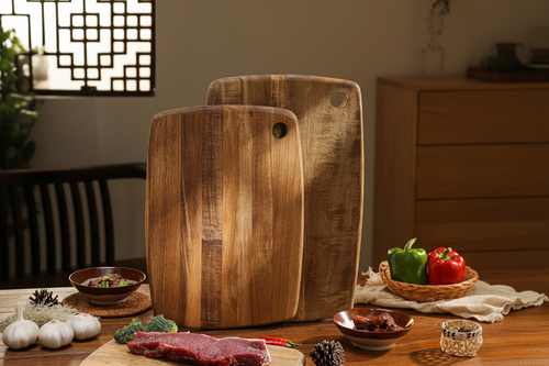 Two acacia wood cutting boards with rounded corners and hanging holes displayed upright in a kitchen.
