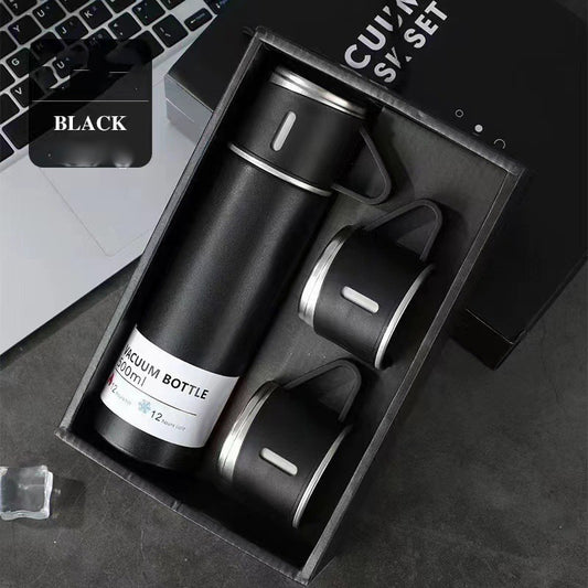 Black vacuum flask with a matching handled cup on top and two additional cups arranged in a black gift box.