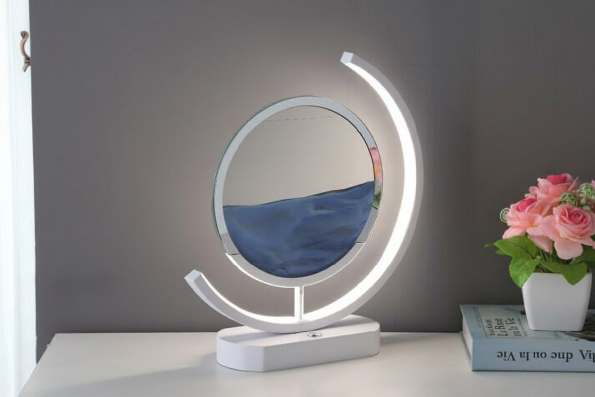 Angled view of a blue sand art table lamp showing its circular display, illuminated curved frame, and white base.