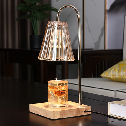 Candle warmer lamp with a ribbed shade illuminating a decorative jar candle on a wooden base beside a sofa.