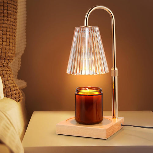 Illuminated candle warmer lamp with a curved gold-tone stem and wooden base over an amber candle jar on a bedside table.