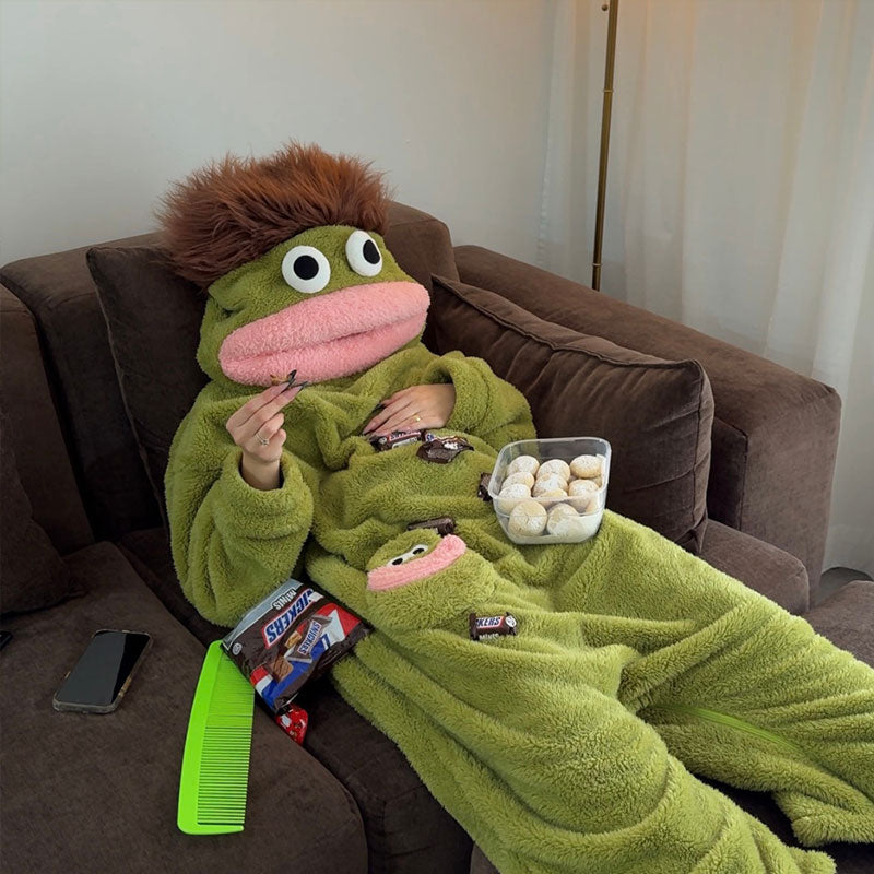 Person reading on the floor in green plush fish onesie pajamas inside a cozy living room.