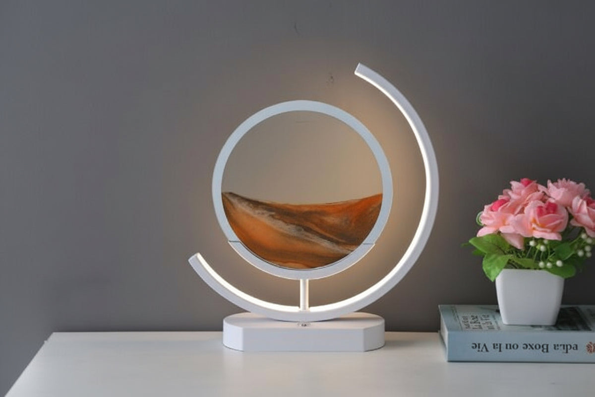 Round golden brown sand art display inside a white table lamp with an illuminated curved frame.