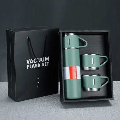 Green vacuum flask and three matching handled cups displayed in an open gift box beside a black gift bag.