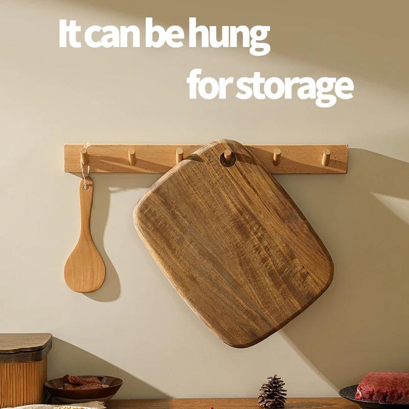 Acacia wood cutting board hanging from a wall rack by its built-in storage hole.