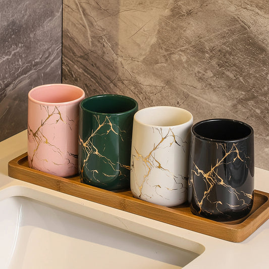 Four different ceramic tumblers sitting on a wooden plate in the bathroom on top of the sink.