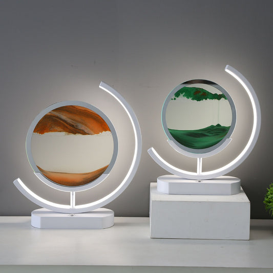 Two white table lamps with illuminated curved frames surrounding round sand art displays in golden brown and green.