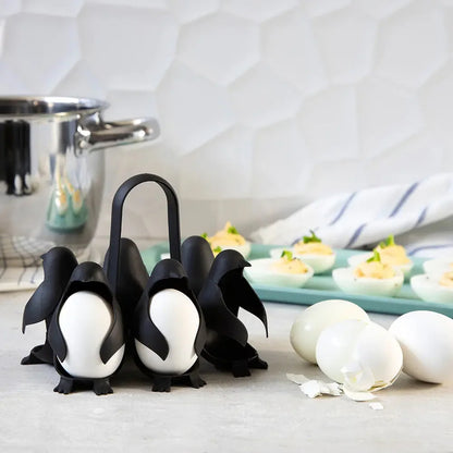 Penguin-shaped egg holder with white eggs on a kitchen counter beside cracked eggshells and a tray of deviled eggs.