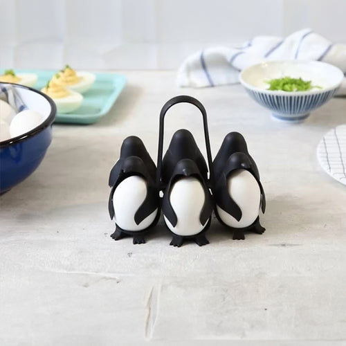 Black penguin-shaped egg holder holding white eggs, with a central loop handle, on a kitchen countertop.