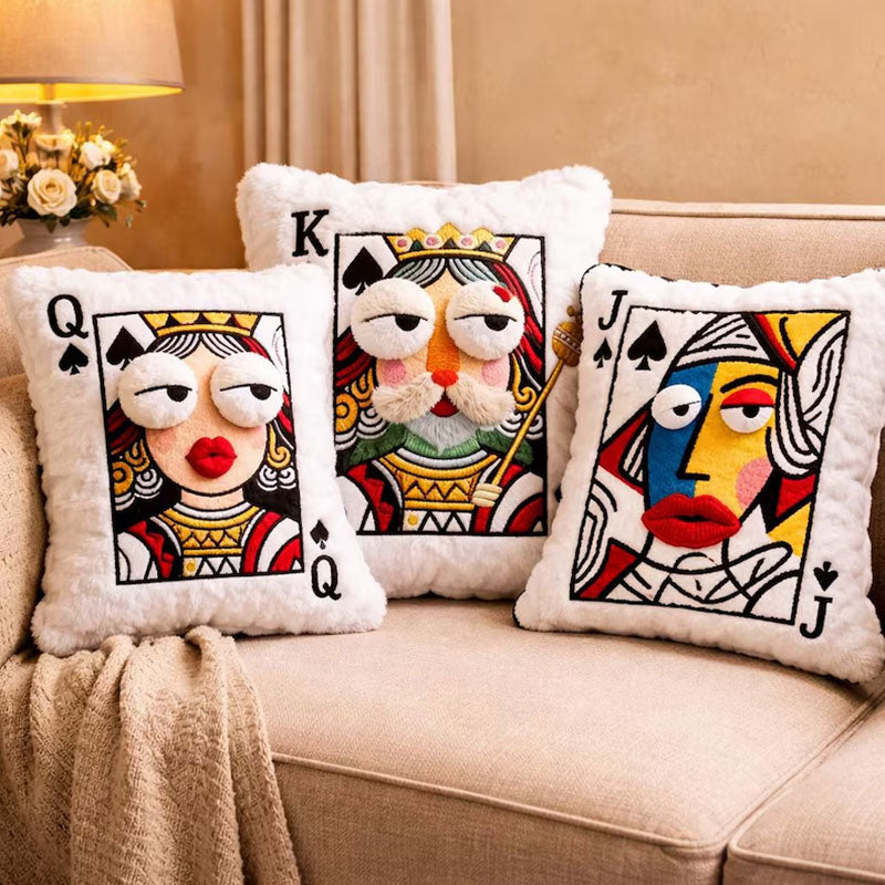 Queen, King, and Jack embroidered playing card throw pillows arranged together on a beige sofa.
