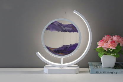 Purple sand falling inside a round sand art display with an illuminated white curved frame and matching base.