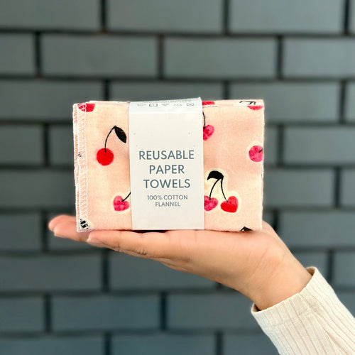 Reusable paper towels with cherry design held by a person against a brick wall.