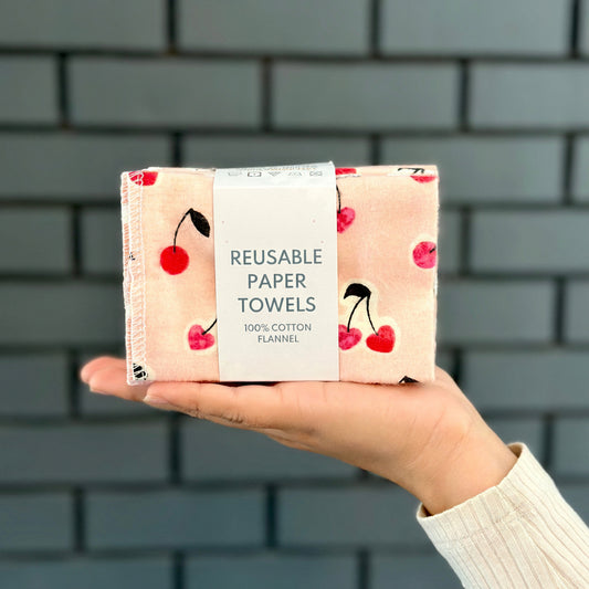 Reusable paper towels with cherry design held by a person against a brick wall.