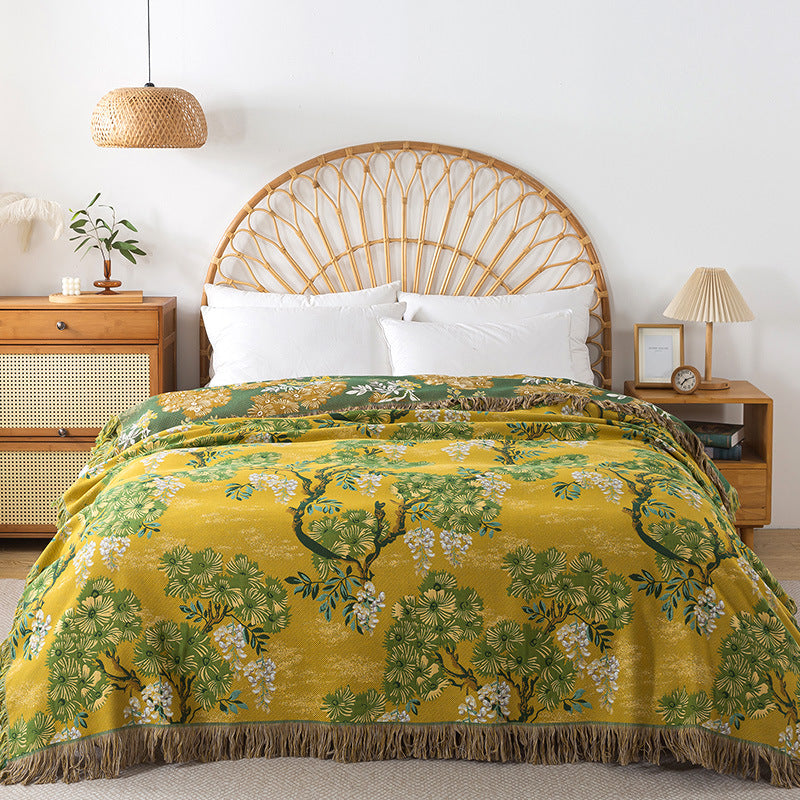 Yellow and green reversible cotton blanket with a detailed botanical jungle pattern and fringed edge displayed on a bed.