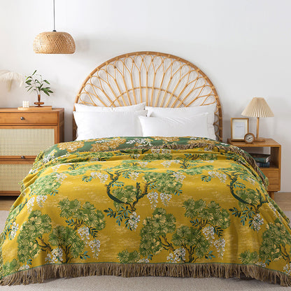 Yellow and green reversible cotton blanket with a detailed botanical jungle pattern and fringed edge displayed on a bed.