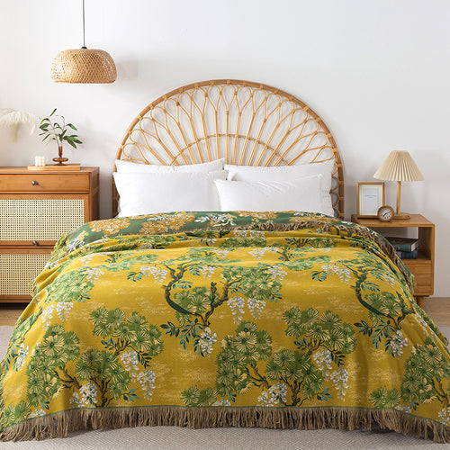 Yellow and green reversible cotton blanket with a detailed botanical jungle pattern and fringed edge displayed on a bed.
