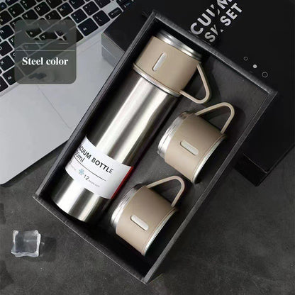 Silver-colored vacuum flask with a beige handled cup on top and two matching cups arranged in a black gift box.