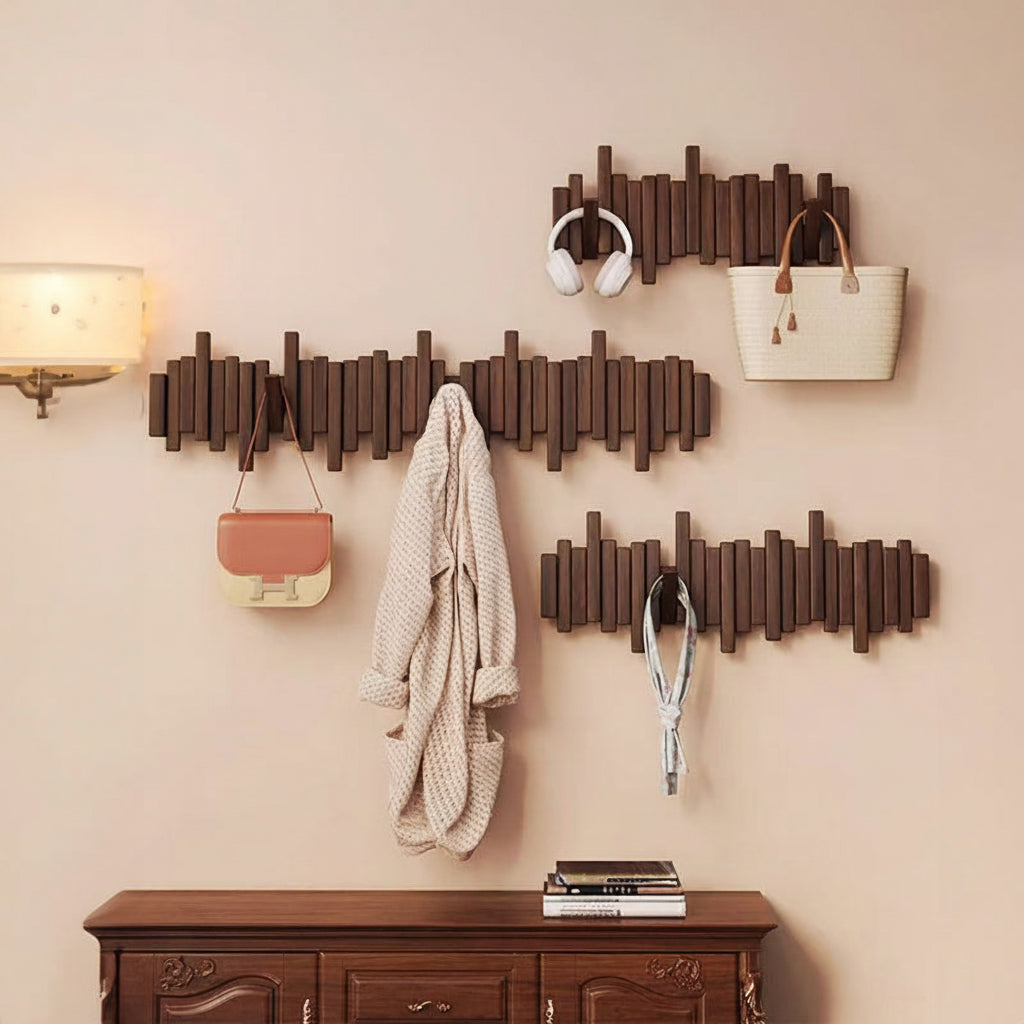 Three Wooden wall mounted coat racks with hooks holding bags, headphones, clothing, and accessories in an entryway with a bench in the middle