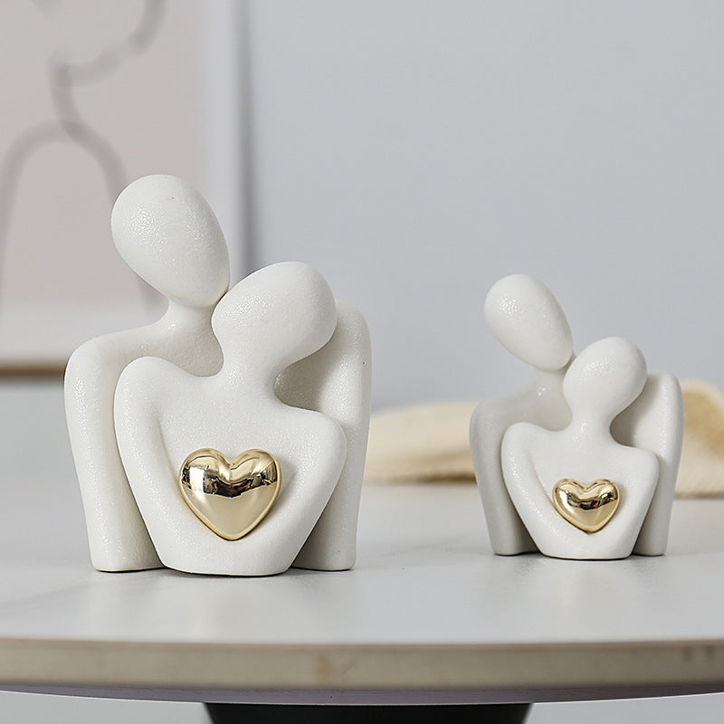 Two white ceramic couple sculptures in different sizes, each with abstract embracing figures and a gold-colored heart.