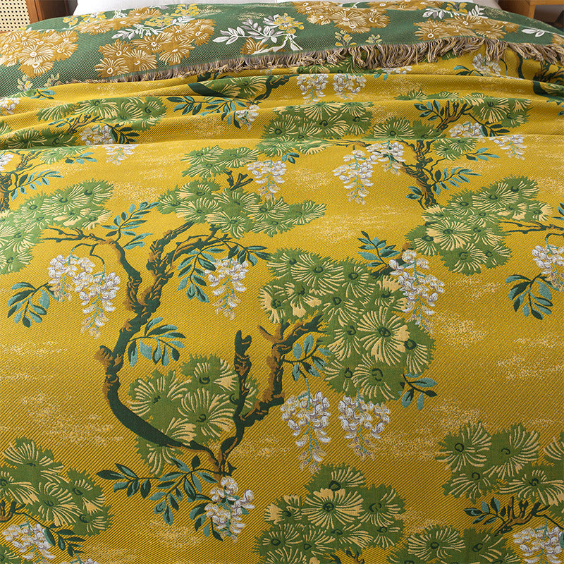 Yellow cotton blanket with green trees, leaves, and white floral details spread across a bed.