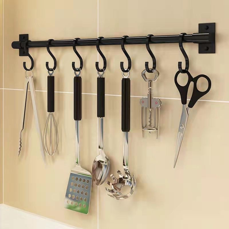 Close-up of a black kitchen utensil rack with seven hooks holding tongs, a whisk, cooking utensils, a corkscrew and scissors.