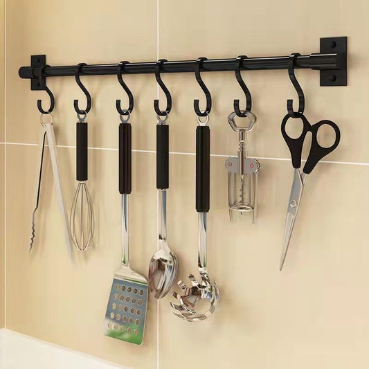 Close-up of a black kitchen utensil rack with seven hooks holding tongs, a whisk, cooking utensils, a corkscrew and scissors.