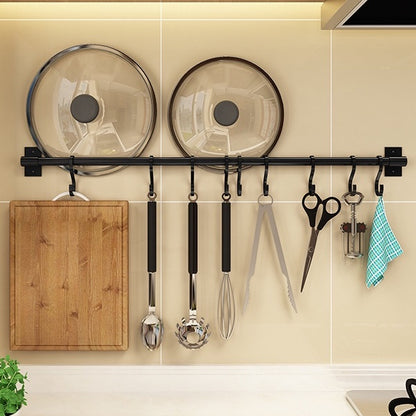 Black wall-mounted kitchen rack with hanging utensils and a cutting board, with two pot lids above the rail.