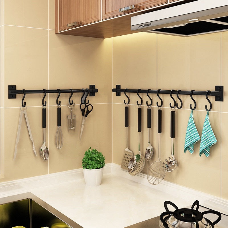 Two black utensil racks mounted on tiled kitchen corner walls, holding cooking tools and dish towels.