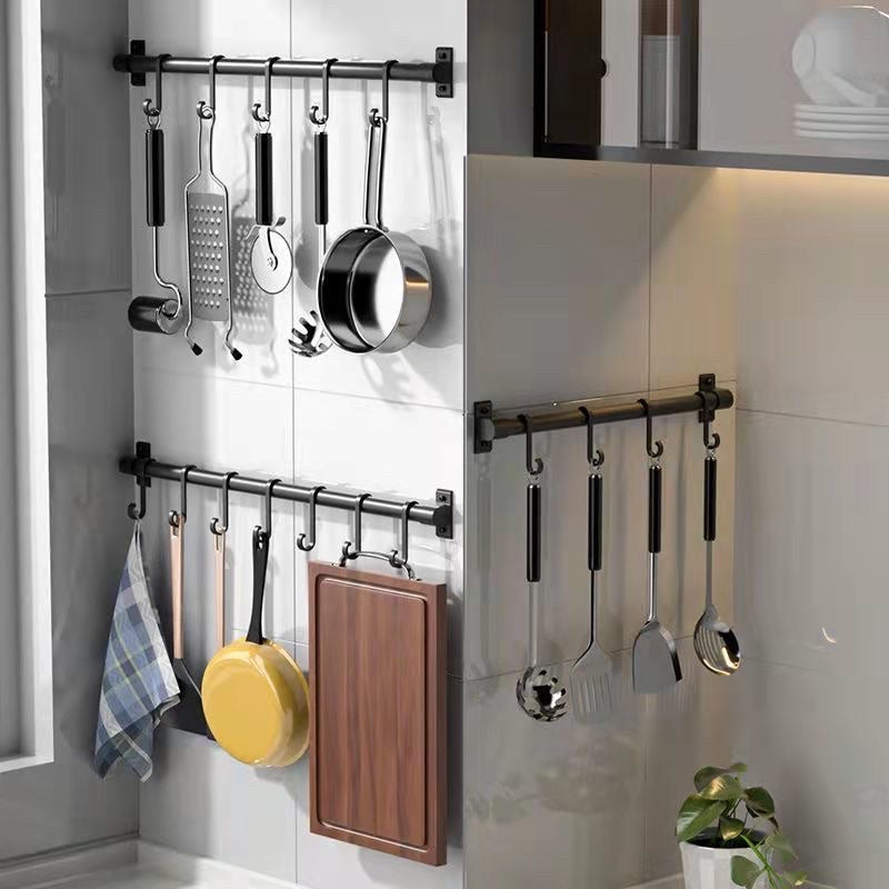 Three black wall-mounted kitchen racks displaying utensils, pans, a cutting board and a dish towel.
