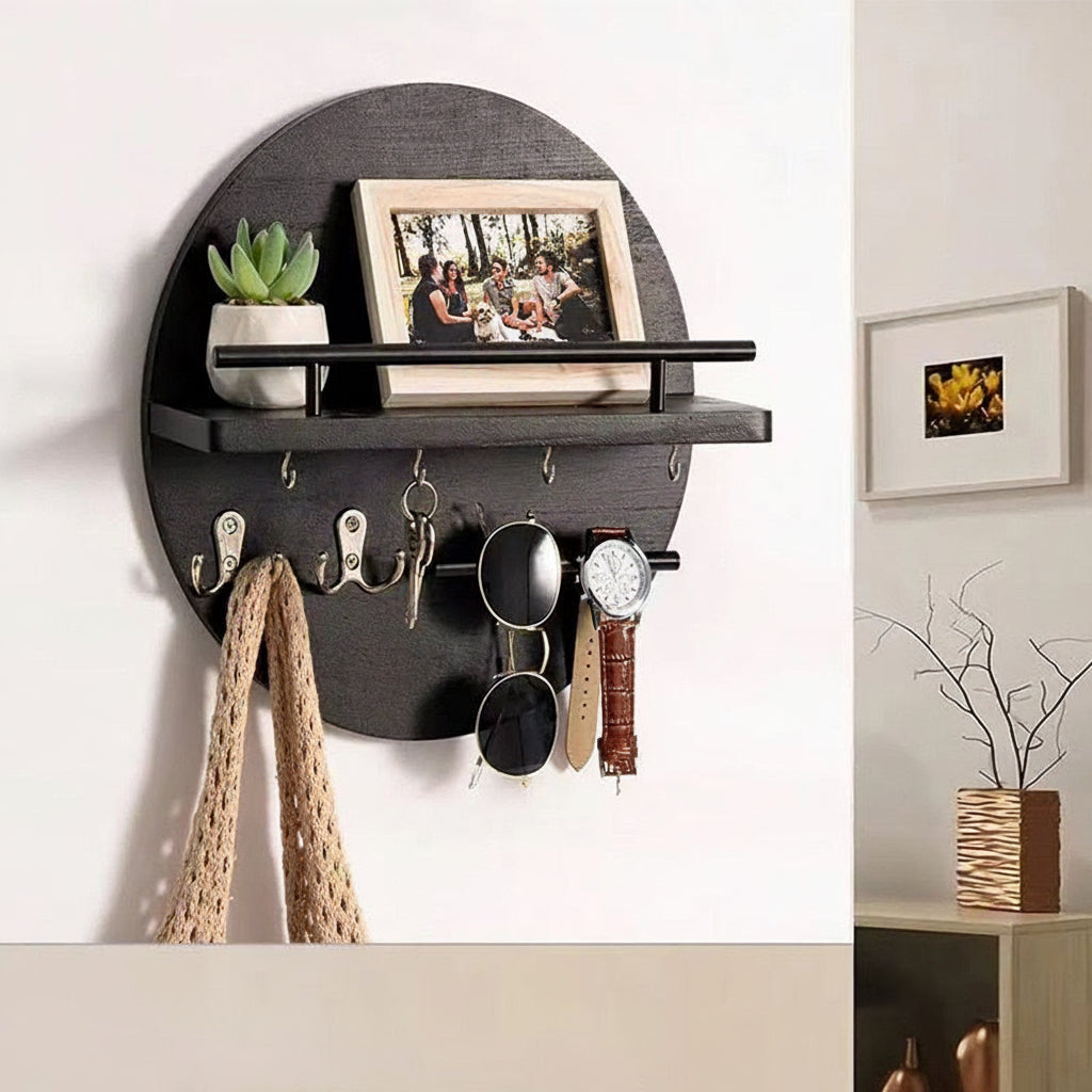 Black round wall-mounted entryway shelf with hooks holding a scarf, keys, sunglasses, and a watch