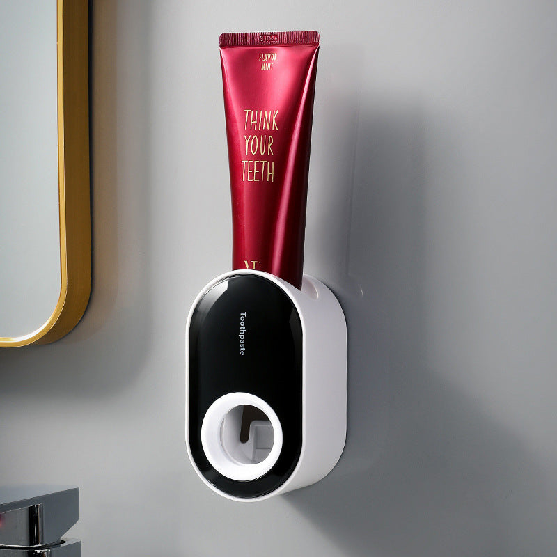 Black and white wall-mounted toothpaste dispenser holding a red toothpaste tube.
