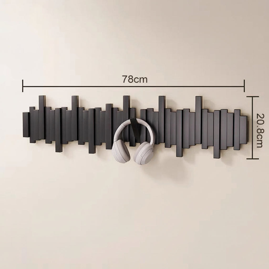 Black wooden wall mounted coat rack with hooks holding white headphones in an entryway