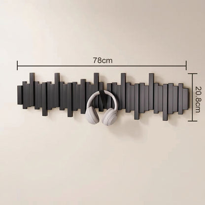 Black wooden wall mounted coat rack with hooks holding white headphones in an entryway