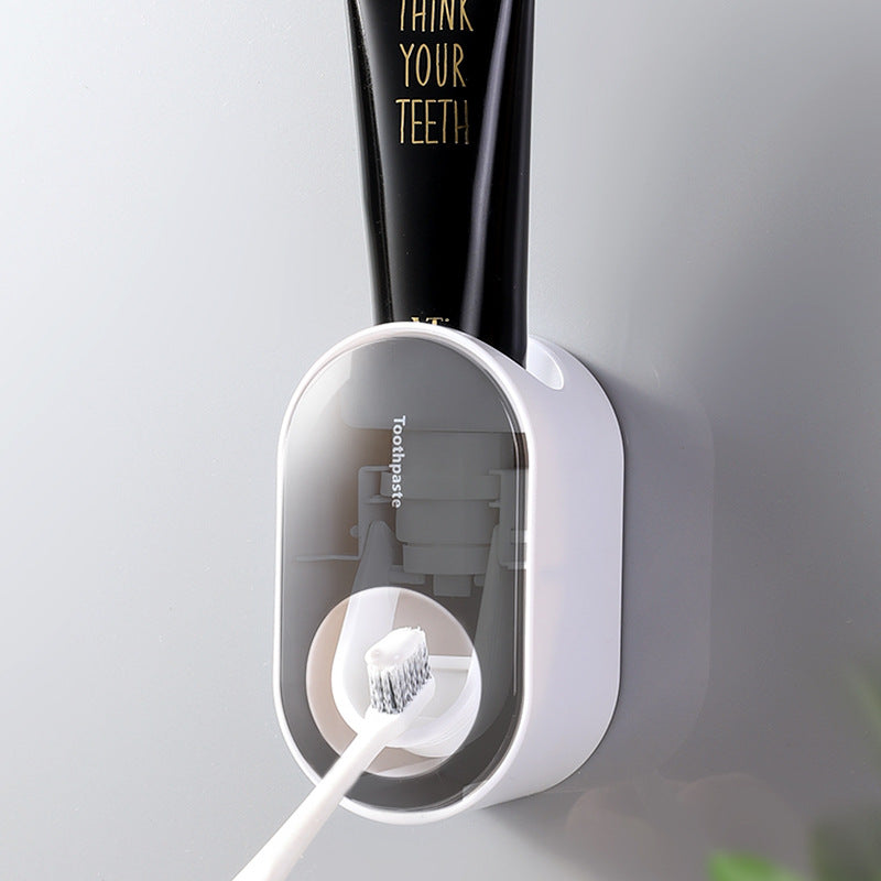Gray wall-mounted toothpaste dispenser applying toothpaste to a toothbrush.