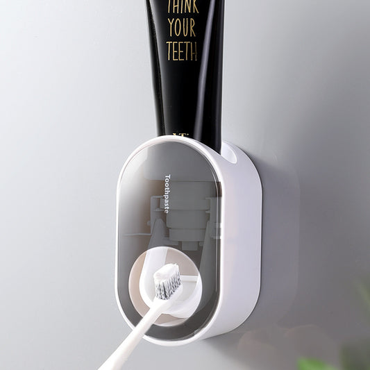 Gray wall-mounted toothpaste dispenser applying toothpaste to a toothbrush.