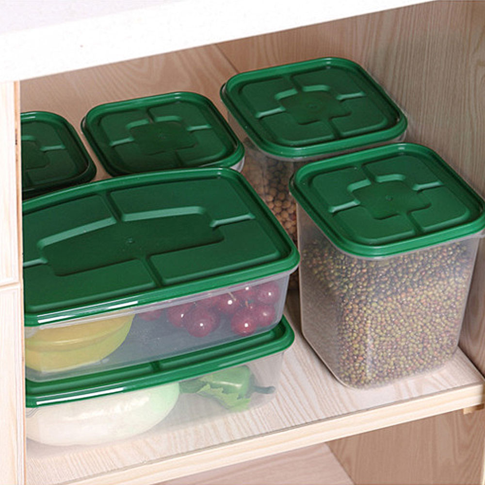 Green-lid stackable food storage containers organizing grains and fruit inside a kitchen cabinet.