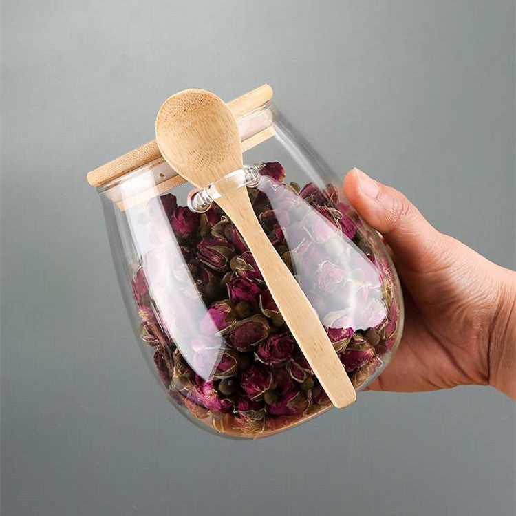 Hand holding a glass spice jar filled with dried rose petals with a bamboo lid and spoon
