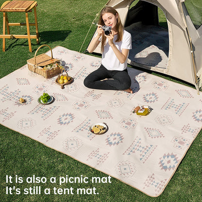 Large patterned picnic blanket spread on grass beside a tent with food and outdoor accessories