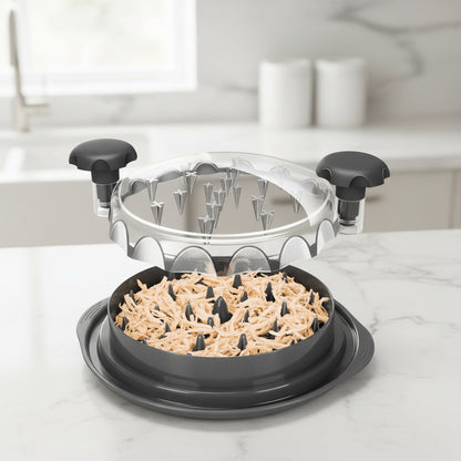 Black manual chicken shredder with handles and clear lid filled with shredded chicken