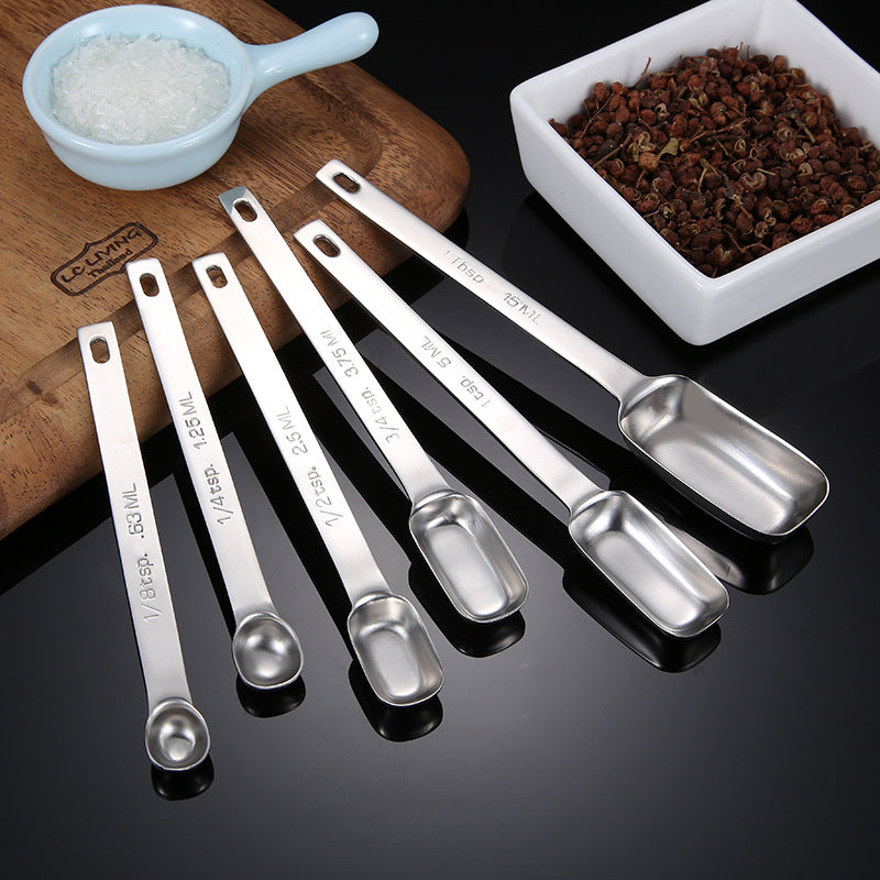 Stainless steel measuring spoon set displayed beside baking ingredients
