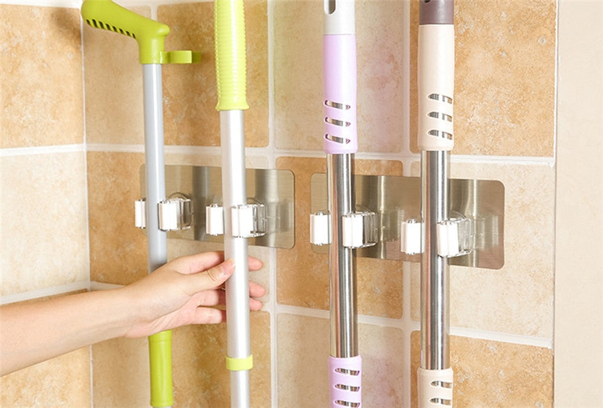 Wall-mounted holders organizing mops and cleaning tools on a tiled utility-room wall.