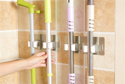 Wall-mounted holders organizing mops and cleaning tools on a tiled utility-room wall.