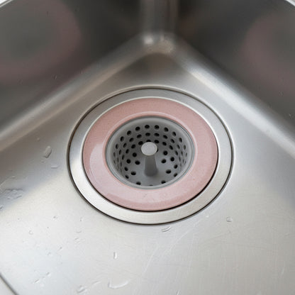 Pink silicone sink drain strainer fitted over a stainless steel kitchen sink drain.