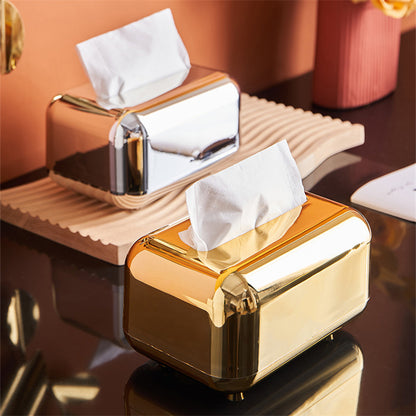 Silver and gold tissue boxes with rounded corners and reflective finishes, displayed together on a table.
