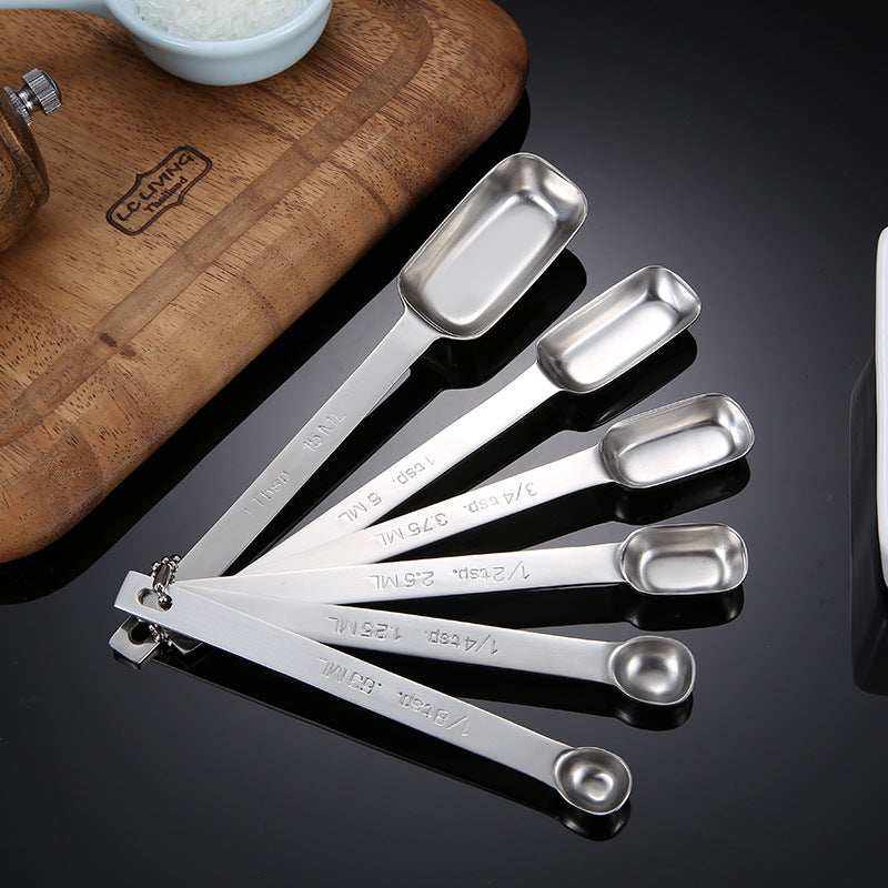 Six stainless steel measuring spoons fanned out on a dark kitchen surface