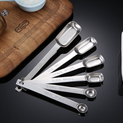 Six stainless steel measuring spoons fanned out on a dark kitchen surface