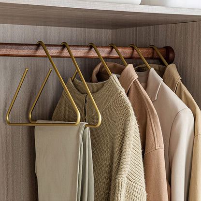 Gold space-saving pants hangers holding trousers and clothing on a wooden closet rod