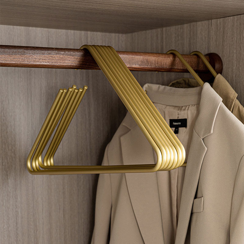 Stack of matte gold aluminum space-saving pants hangers on a wooden closet rod
