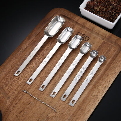 Six stainless steel measuring spoons arranged by size on a wooden cutting board