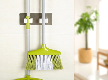 Wall-mounted cleaning tool holder securing a green broom against the wall.